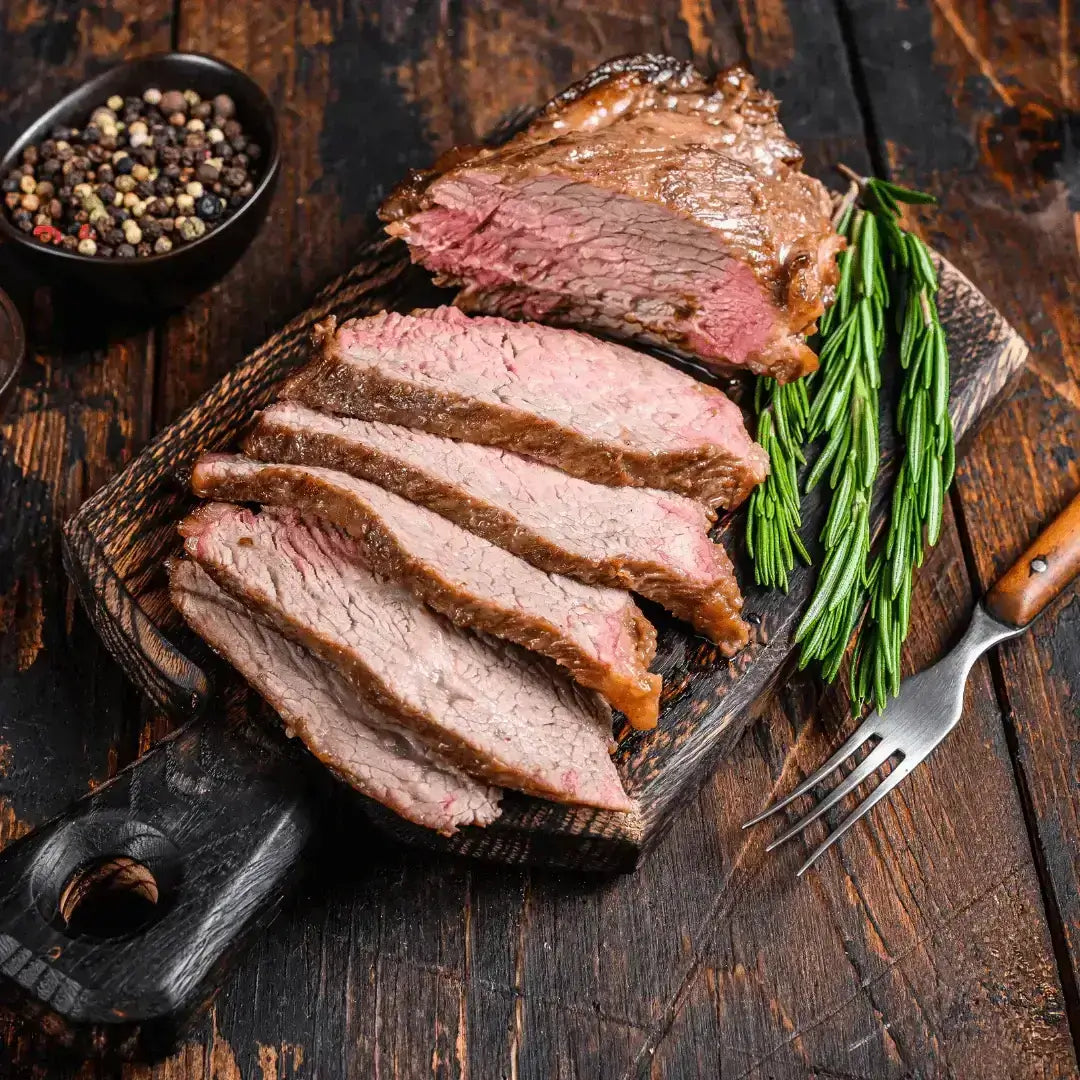 Sliced Reverse Sear Tri Tip on a wooden cutting board with herbs and spices.