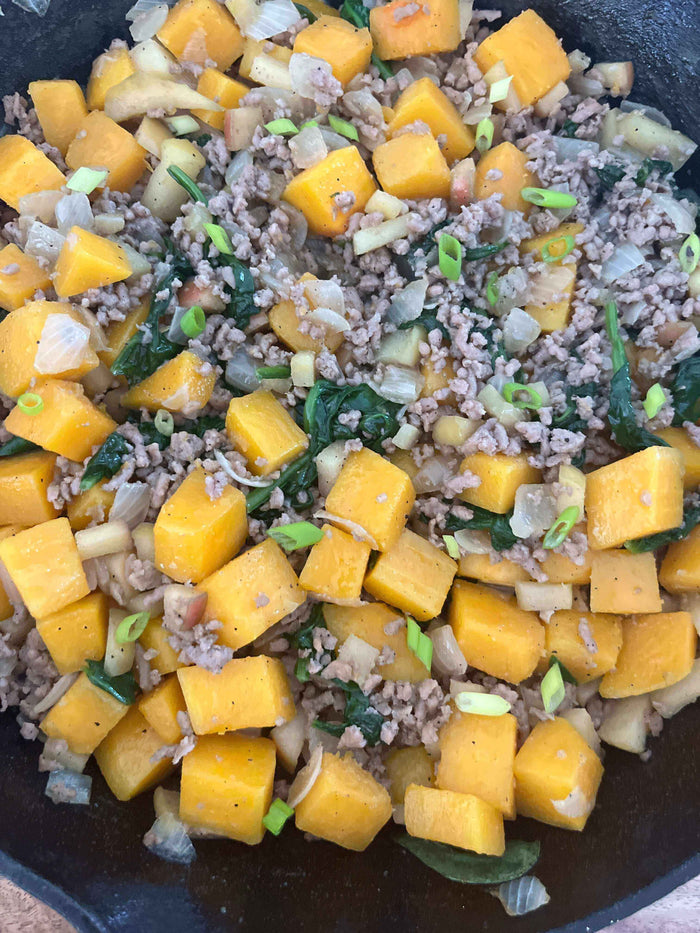 Butternut Squash, Apple, & Sausage Hash in a skillet, showcasing a delicious blend of squash, sausage, and greens.