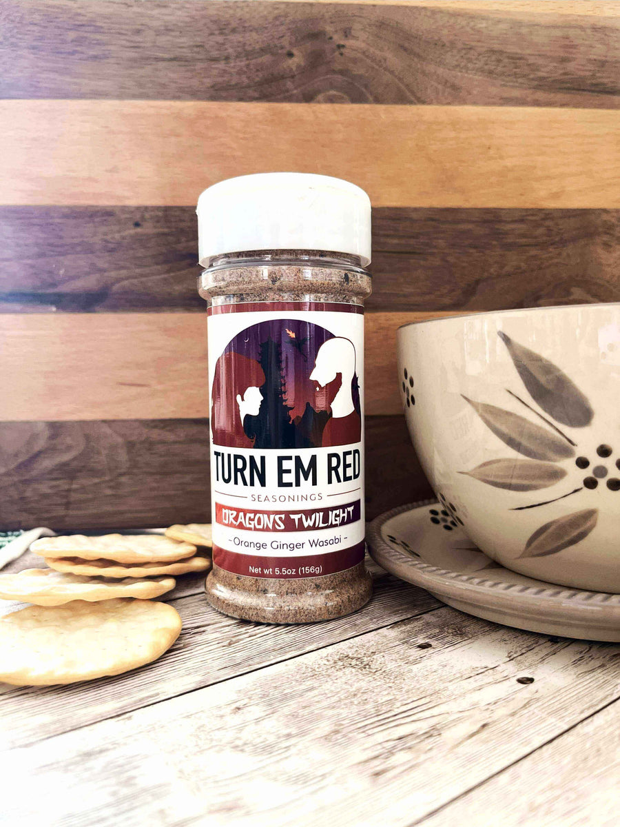 Turn Em Red seasonings with Dragons Twilight label next to a bowl and crackers on a wooden surface.