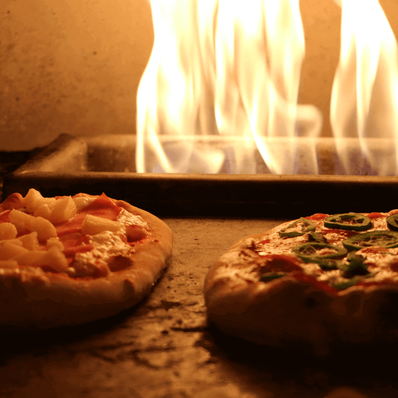 His & Her Ooni Pizza Recipe (feat. Volcanic Sunset) with pizzas baking over an open flame.