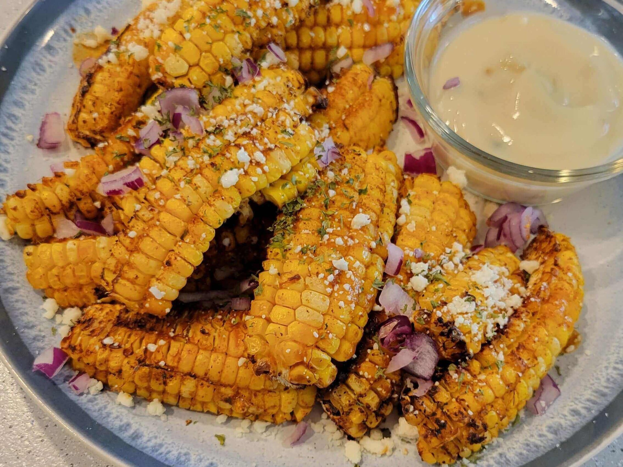 Plate of Spicy Mexican Corn Ribs topped with cheese and onions, served with a creamy dipping sauce.