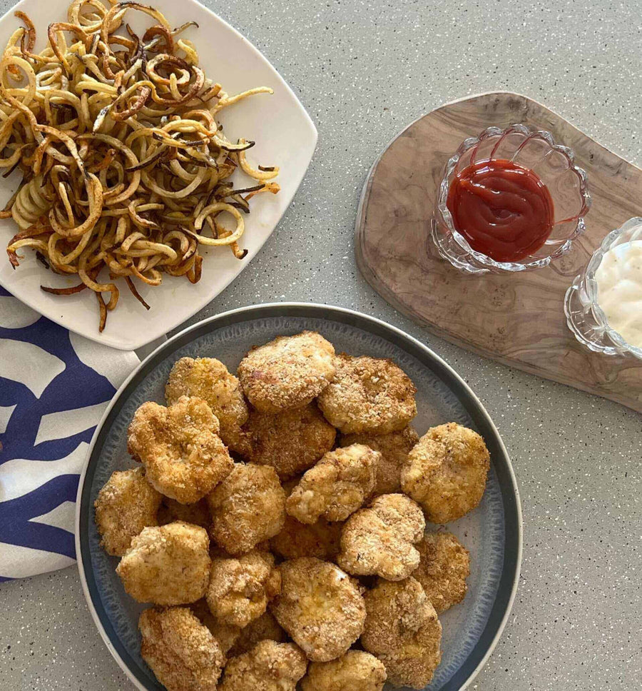 Healthy Chicken Nuggets - Fast Food Style served with spiral fries, ketchup, and creamy dip on a stylish table.