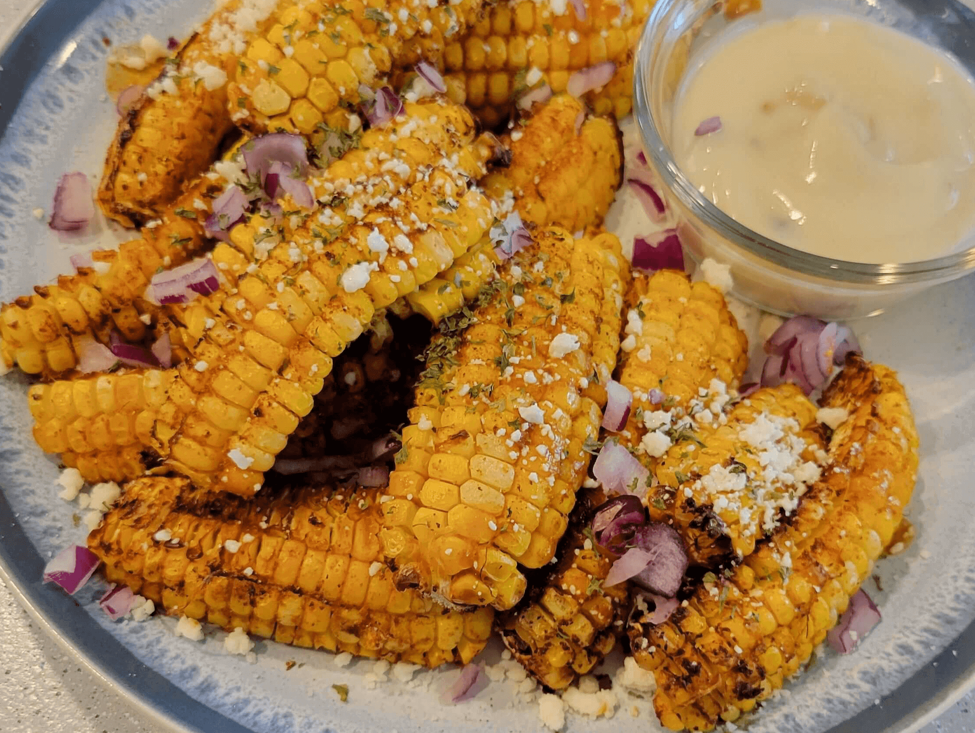 Delicious Spicy Mexican Corn Ribs garnished with onions and served with sauce on a platter.