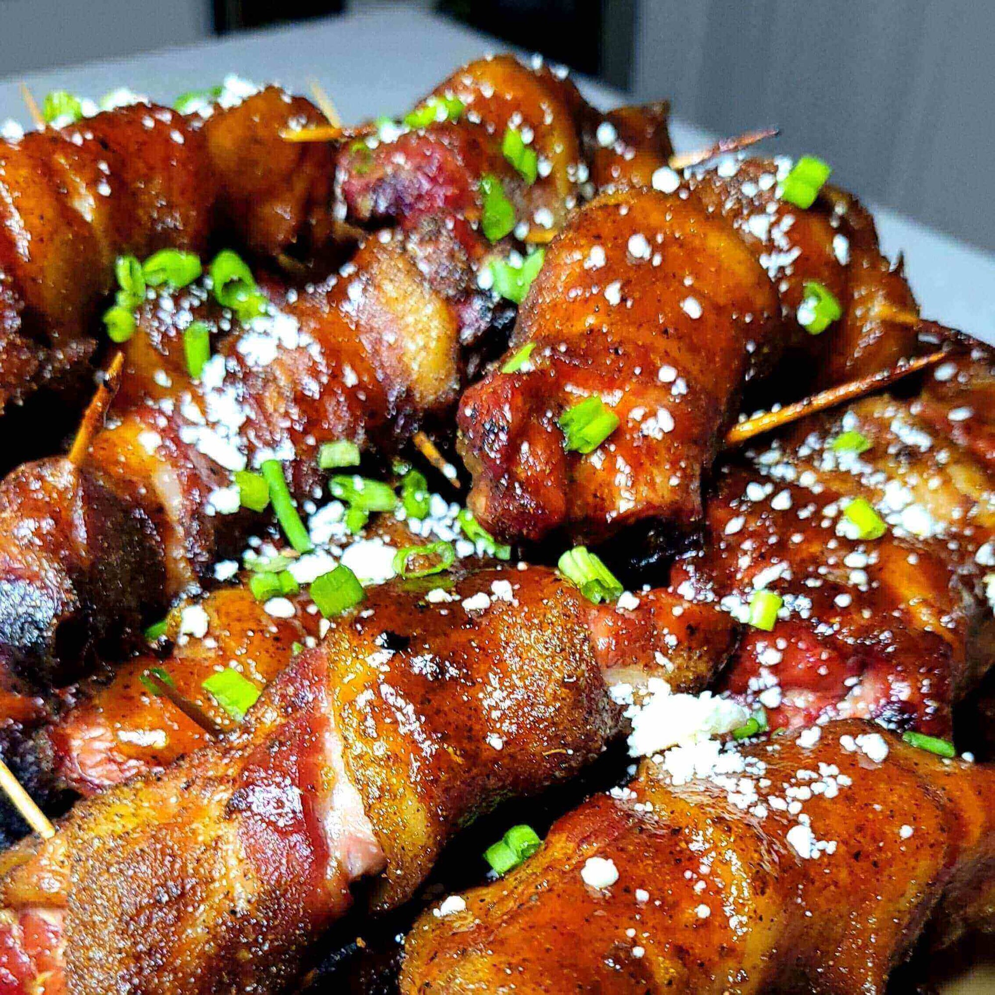 Bacon-Wrapped Ribs: The Porky Showstopper, savory and crispy, garnished with green onions and feta.