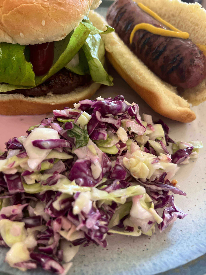 Sweet and Tangy Coleslaw served with a hamburger and hot dog on a plate, perfect for summer barbecues.