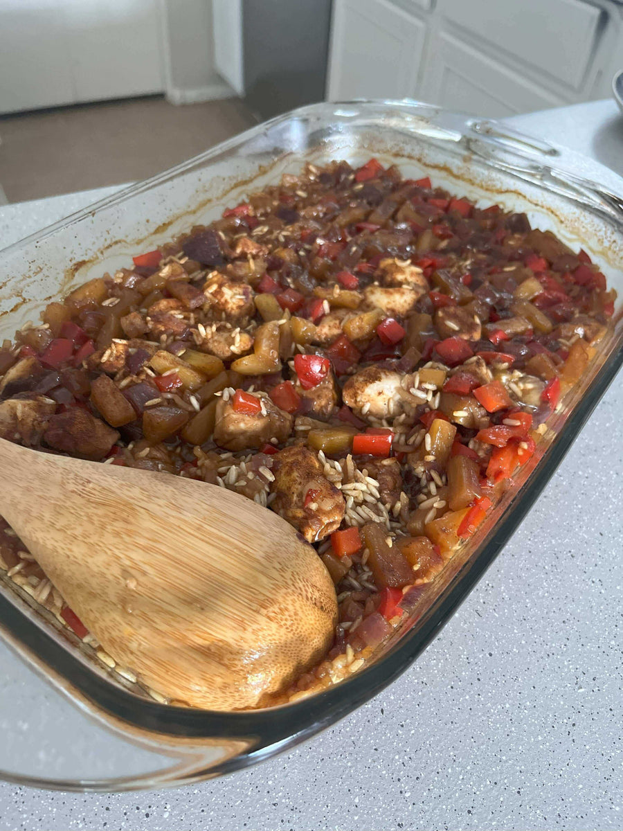 Aloha Chicken Casserole in a baking dish with red peppers, chicken, and a wooden spoon ready to serve.