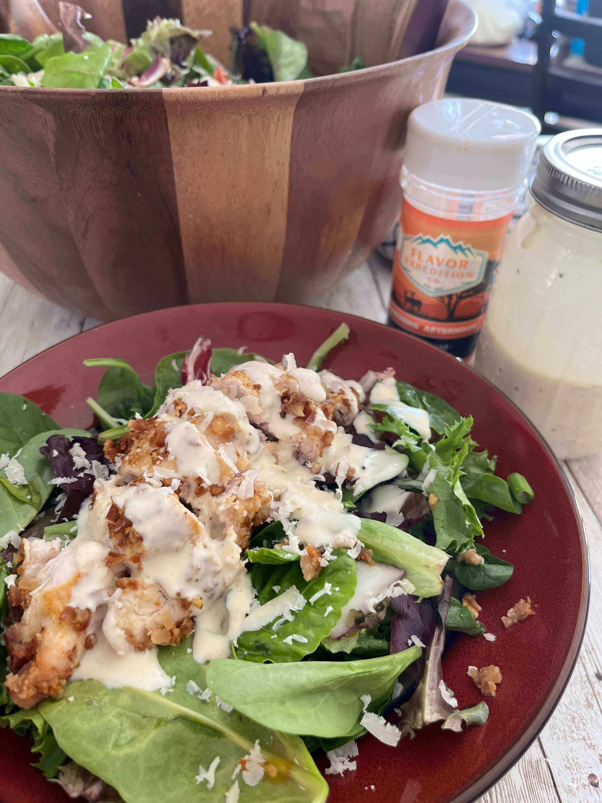Spicy Mustard Pretzel Chicken Salad topped with creamy dressing and crispy chicken on a plate, with a salad bowl in the background.