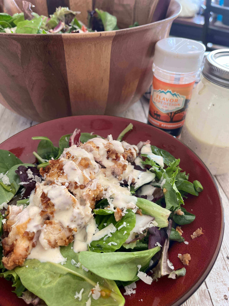 Spicy Mustard Pretzel Chicken Salad topped with creamy dressing and crispy chicken on a plate, with a salad bowl in the background.