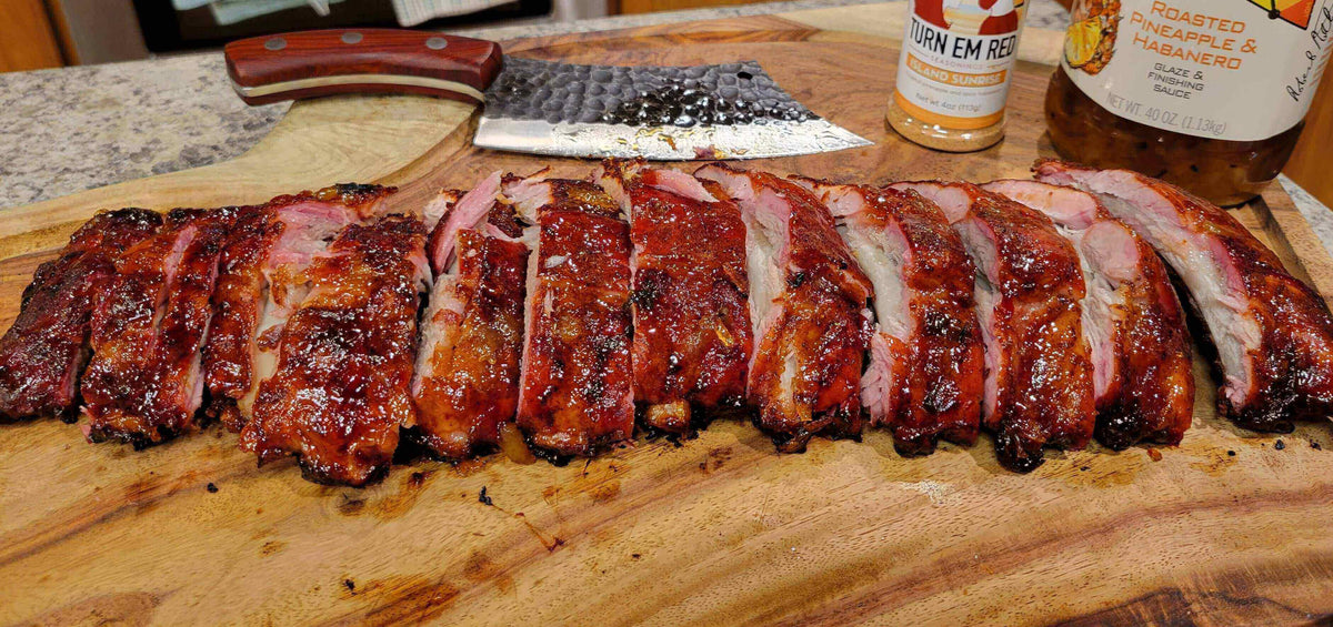 Smoked Pineapple Habanero Ribs laid out on a wooden cutting board with a knife and seasoning nearby.