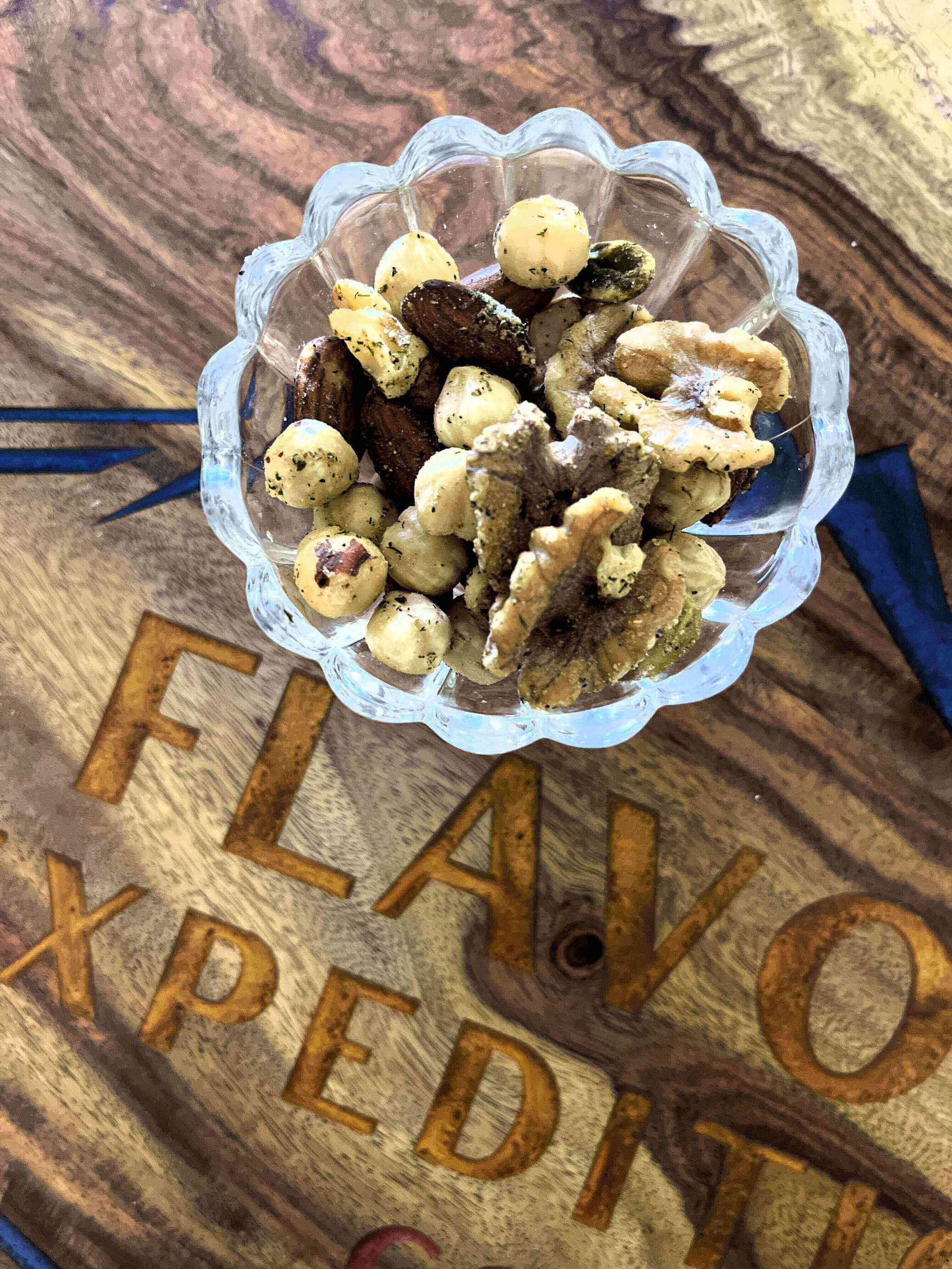 Nut Your Average Snack: Rosemary Red Pepper Parm Spiced Nuts in a glass bowl on a wooden surface.