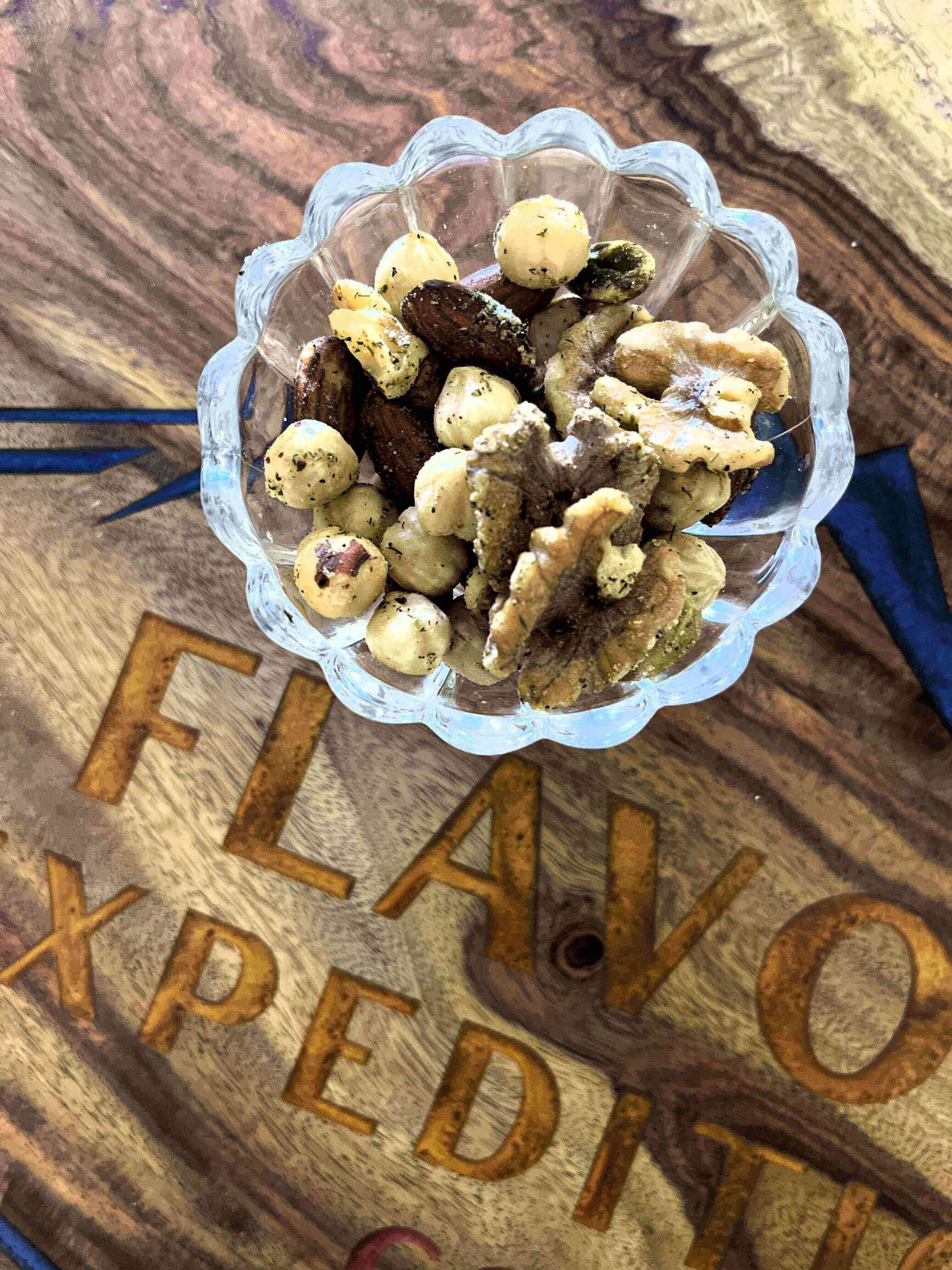Nut Your Average Snack: Rosemary Red Pepper Parm Spiced Nuts in a glass bowl on a wooden table.