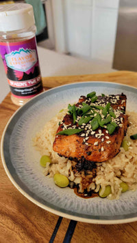 Dragons Twilight Glazed Salmon on rice, sprinkled with green onions and sesame seeds, with seasoning jar in the background.
