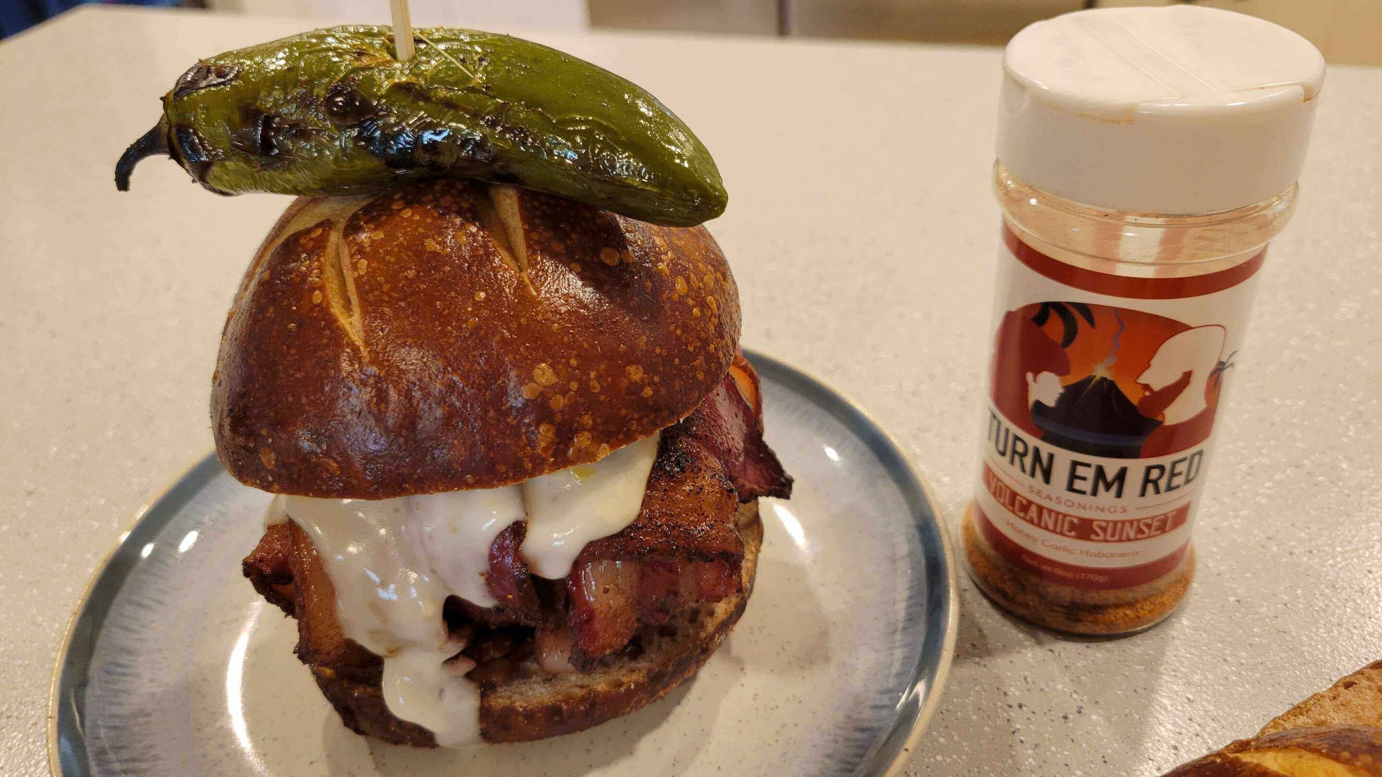 Bacon-Wrapped Smoked Burger Bomb topped with a jalapeño and paired with seasoning on a plate.