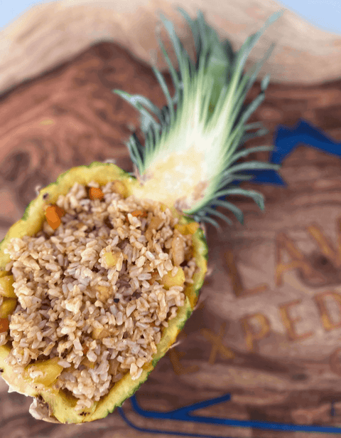 Spicy Pineapple Fried Rice served in a halved pineapple on a wooden board, showcasing vibrant colors and textures.
