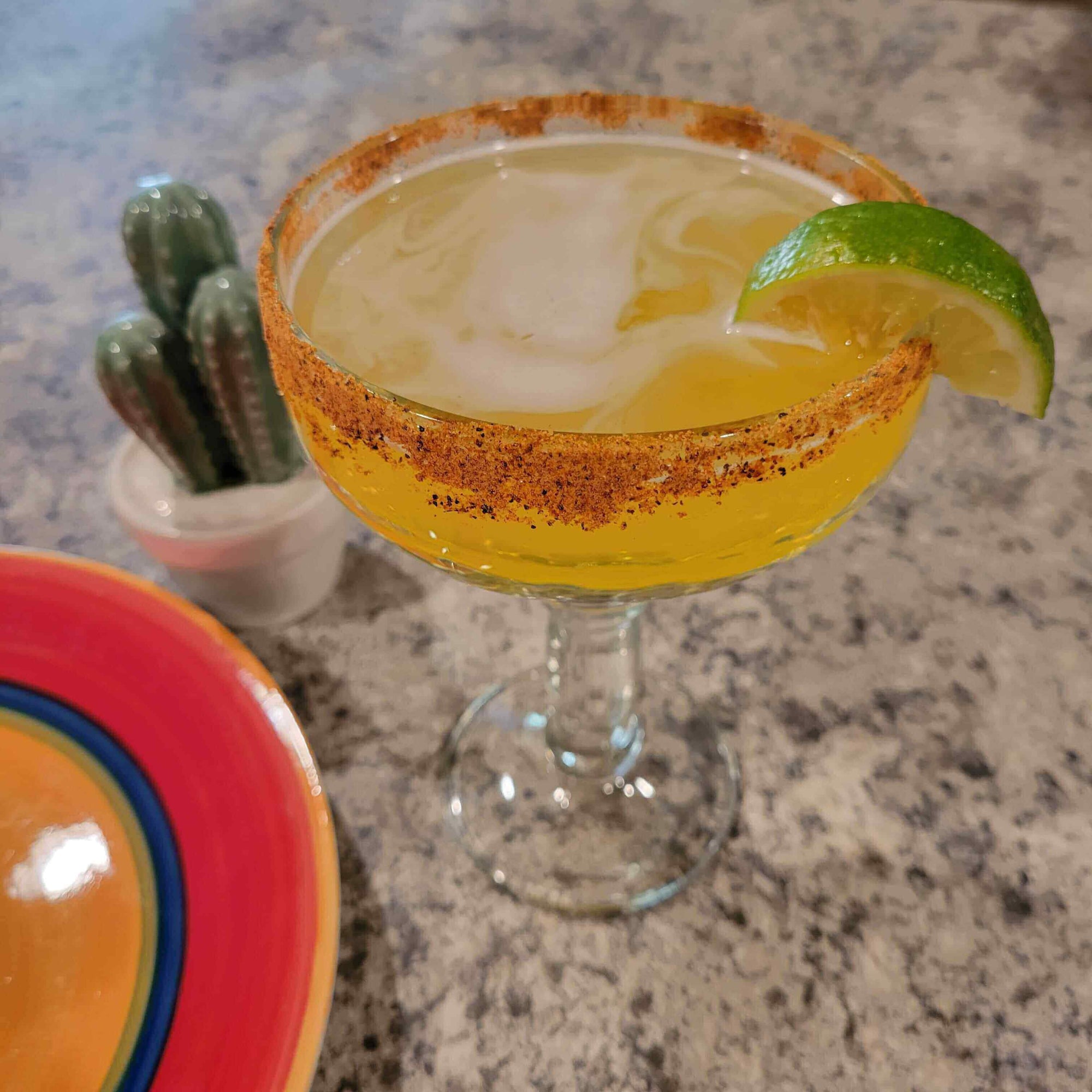 Hot Tropics Margarita garnished with lime and chili-lime rim on a cozy countertop setting.