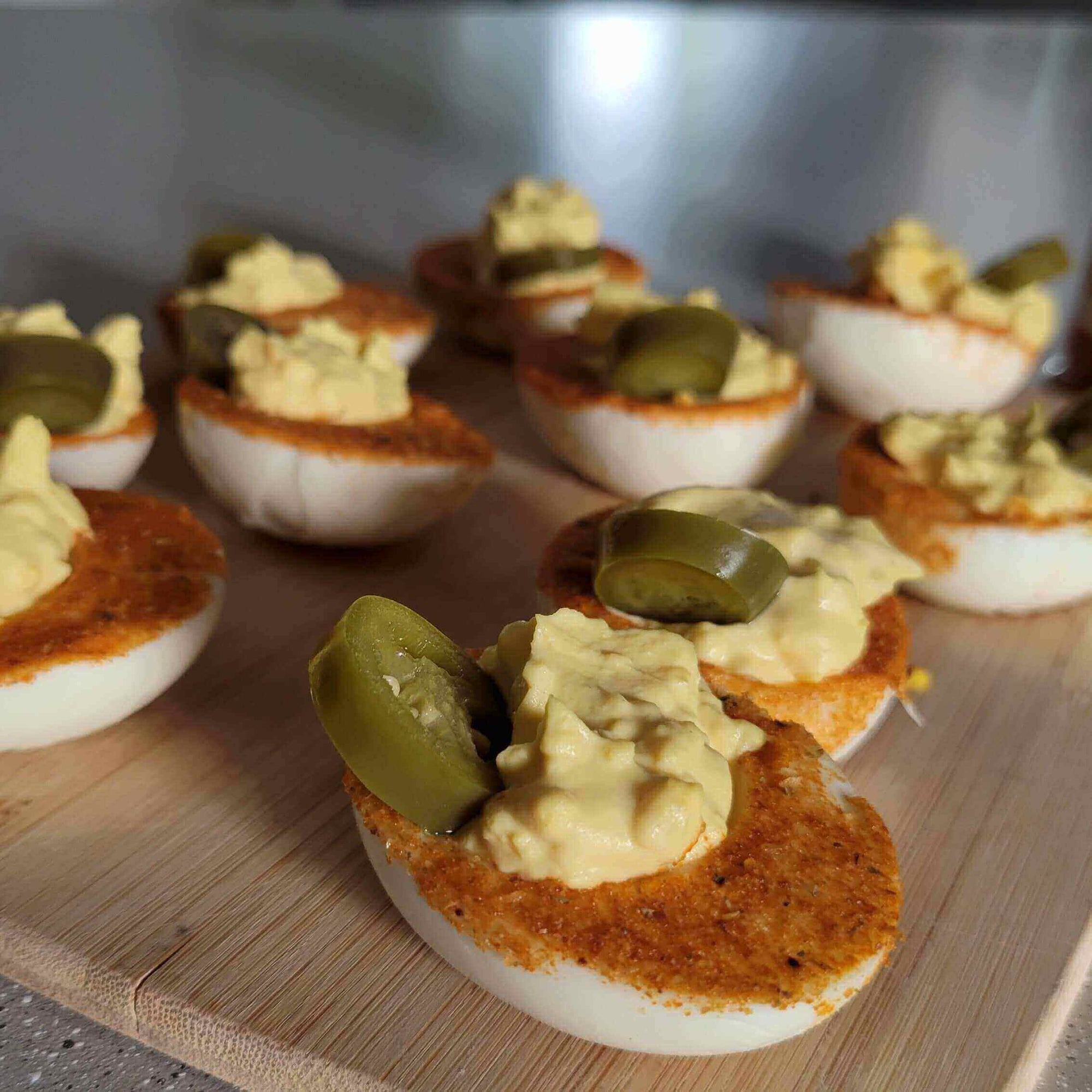 Spicy Mustard Deviled Eggs with a Kick topped with jalapenos on a wooden platter.