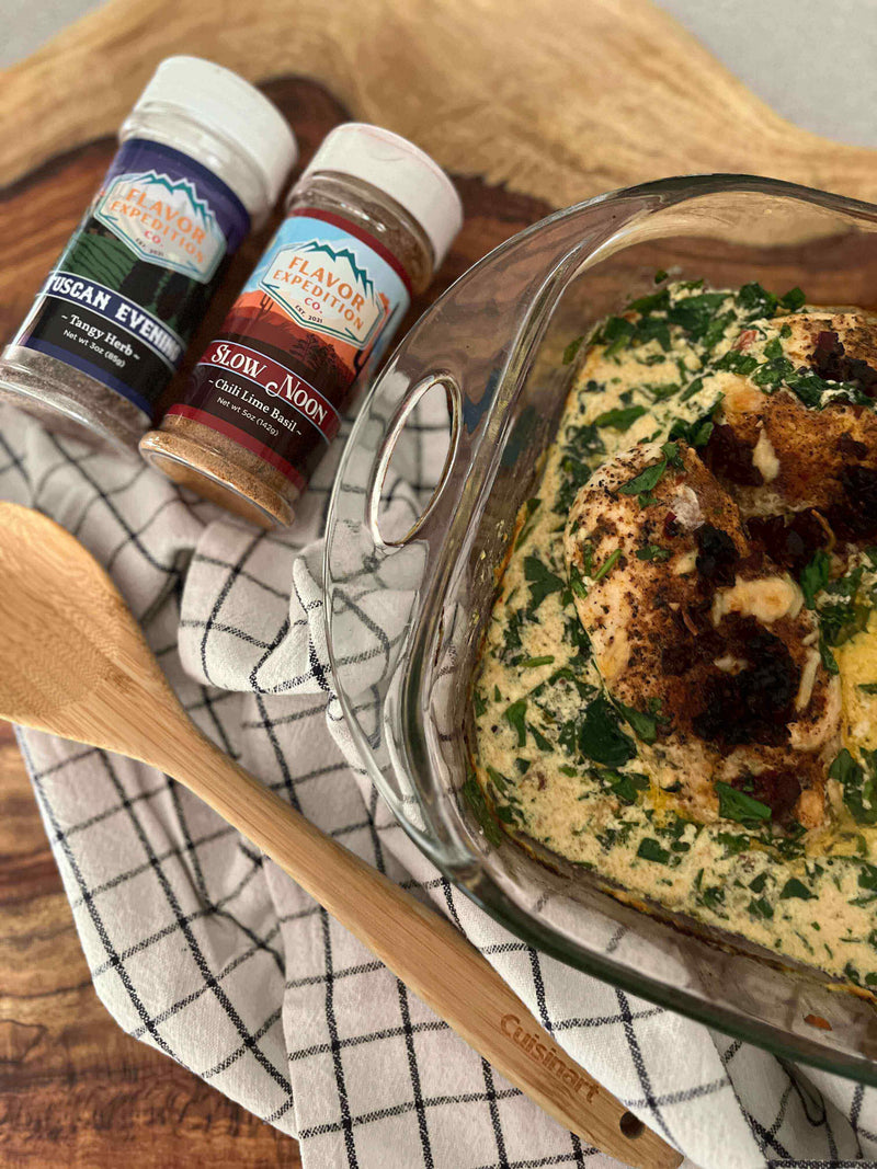 Creamy Baked Tuscan Chicken Breasts in a dish with spices and wooden spoon on a checkered cloth.