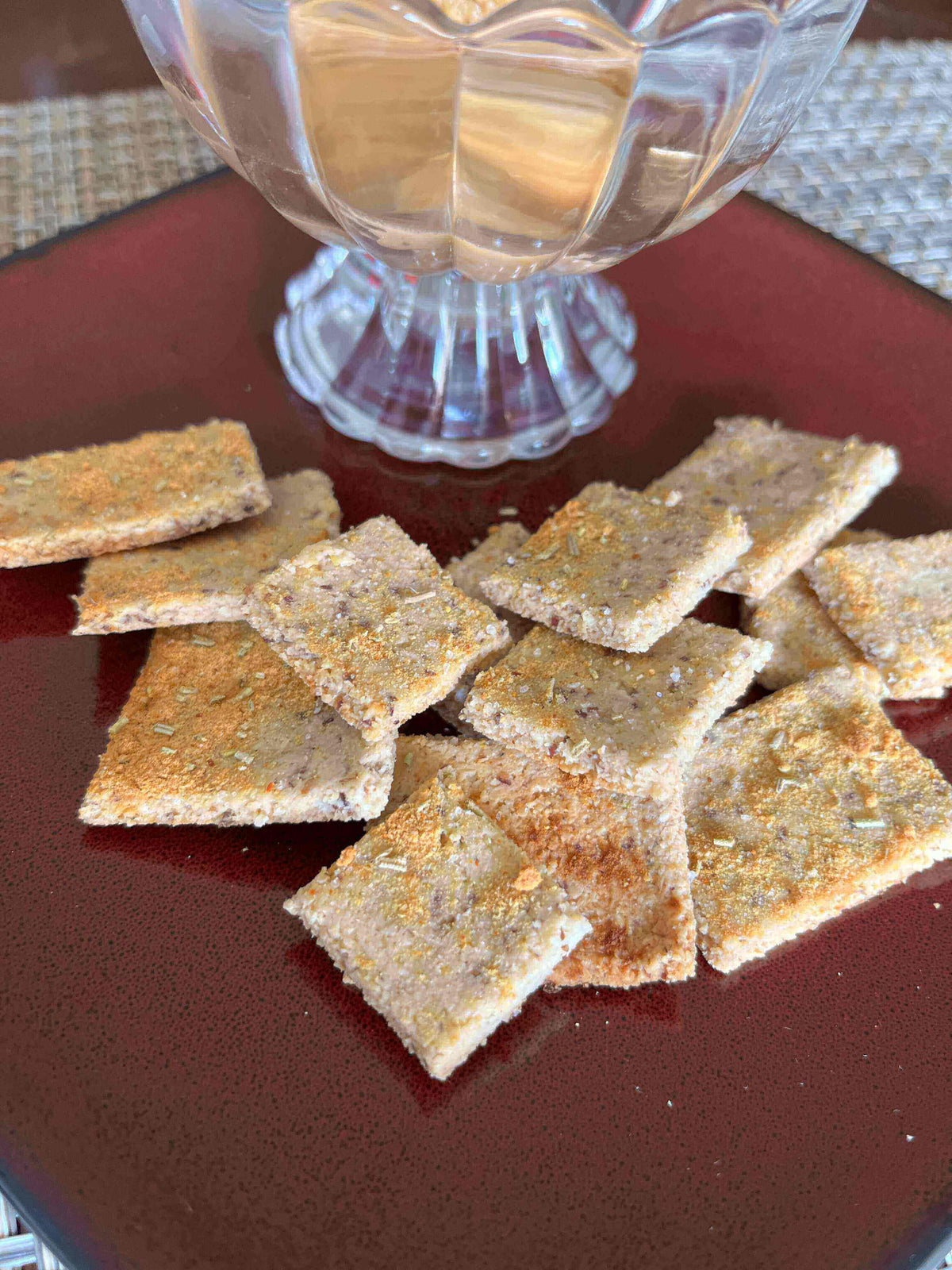 Parmesan Herb Crunchies: Homemade Almond Flour Crackers served with a glass of wine on a red plate.