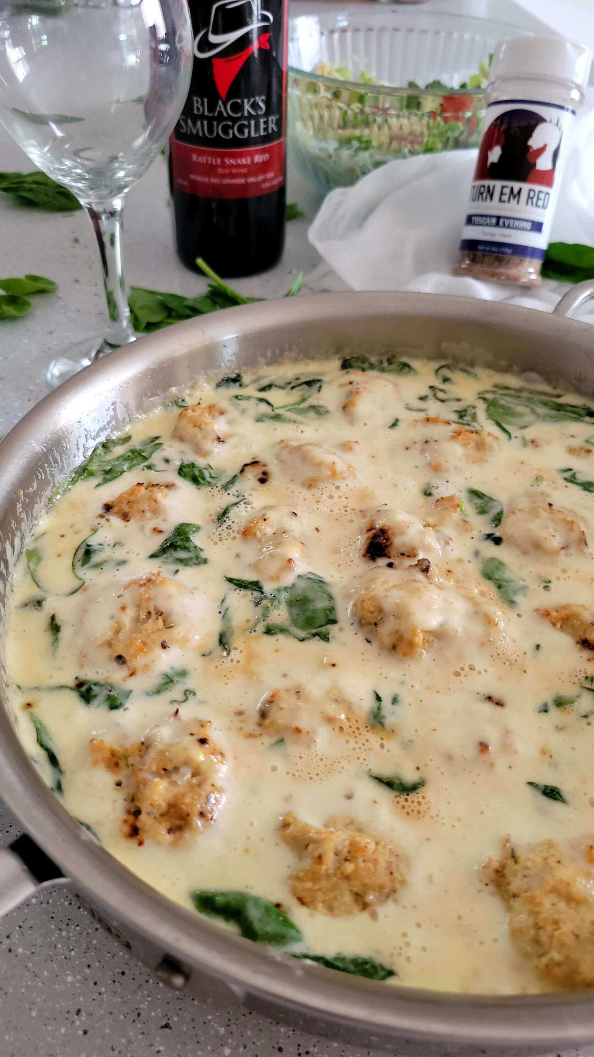 Tuscan Tango Chicken Meatballs in Creamy Alfredo Bliss in a pan, surrounded by fresh ingredients and wine.