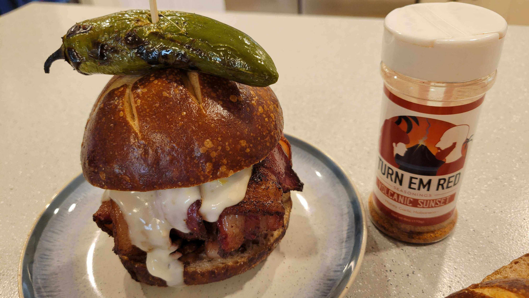 Bacon-Wrapped Smoked Burger Bomb topped with jalapeño, served with seasoning on the side, delicious backyard recipe.
