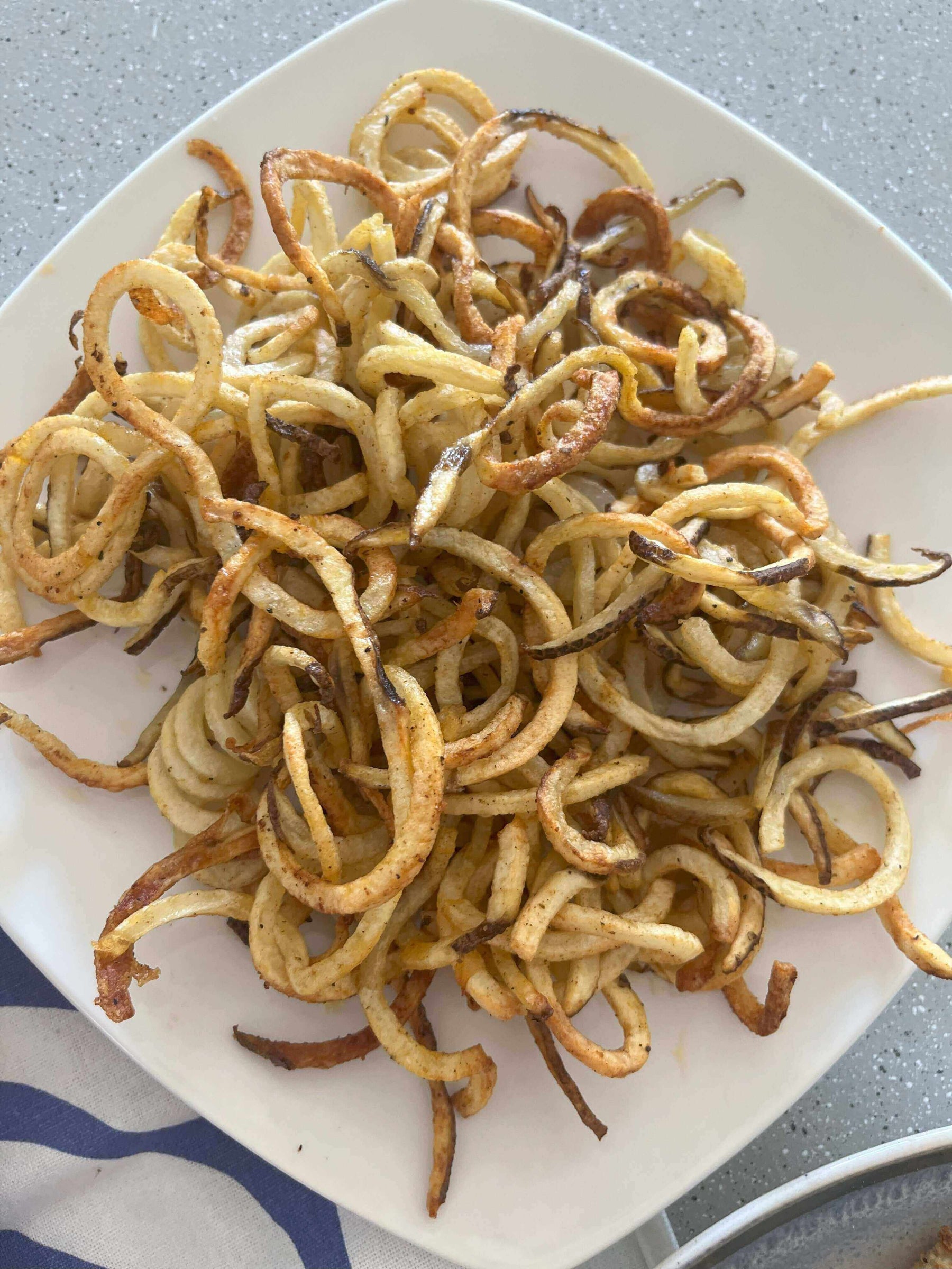 Crispy Air Fryer French Fries piled high on a plate, showcasing their golden crispy texture and curly shape.