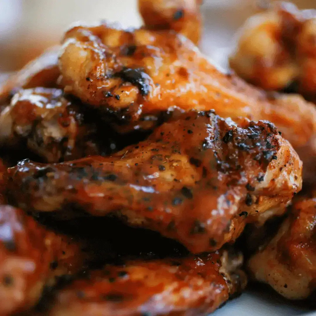 Volcanic Peach Smoked Wings piled high, glistening with smoky glaze and sprinkled with seasoning, ready to devour.