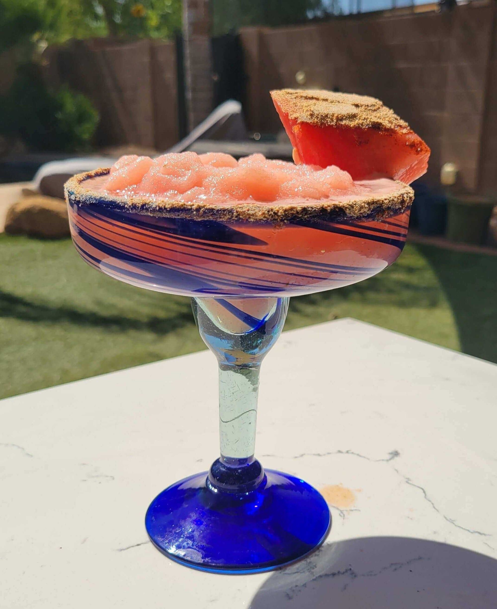 A refreshing Island Time Margarita (aka Watermelon Vacation in a Glass) with a watermelon garnish on a sunny patio.