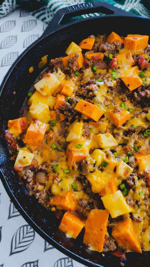 Spicy-Sweet Ground Beef & Sweet Potato Skillet with cheese and green onions in a cast iron pan.