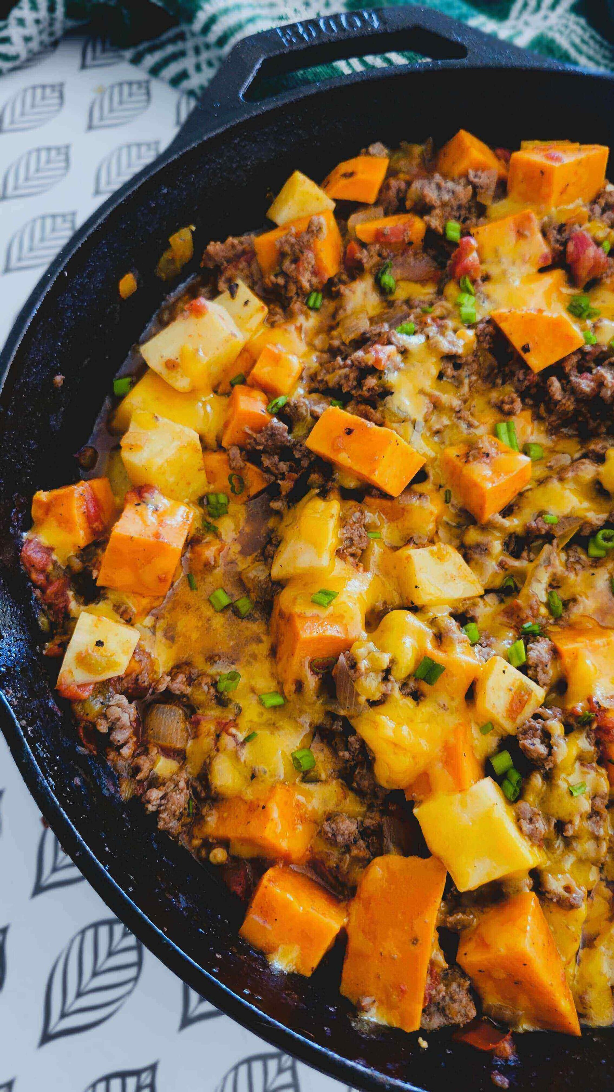 Delicious Spicy-Sweet Ground Beef & Sweet Potato Skillet topped with melted cheese and fresh greens.