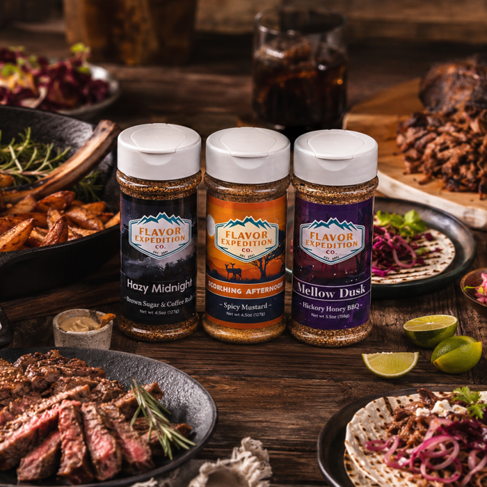 Three jars of Flavor Expedition seasoning on a wooden table with food in the background