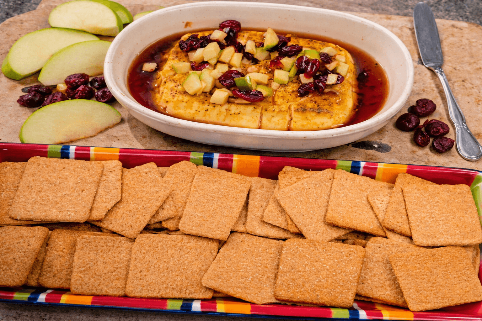 Dip with apples and cranberries served with crackers on a colorful platter.