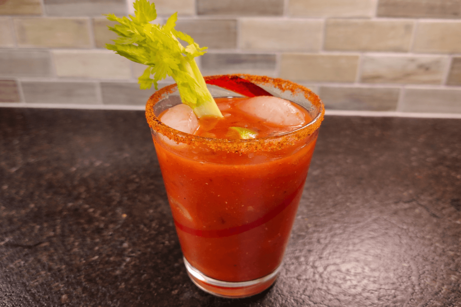 Bloody Mary cocktail with a salt rim and celery garnish on a dark surface.