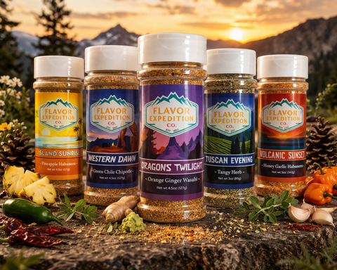 Four jars of Flavor Expedition Co. seasoning blends displayed on a rustic log with fresh herbs, garlic, and peppers, set against a scenic mountain sunset background.