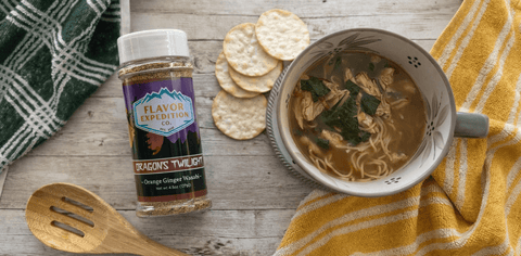 Bowl of soup with crackers and a bottle of seasoning on a wooden surface