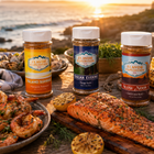 Three jars of 'Flavor Expedition' seasoning on a wooden table with grilled food and sunset over ocean view.