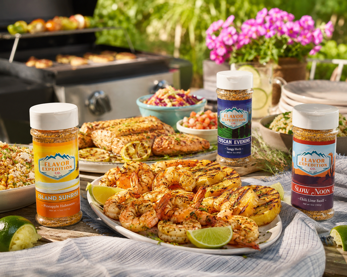 Outdoor setting with grilled food and Flavor Experience seasoning bottles.