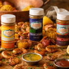Three bottles of Flavor Expedition seasoning on a table with fried food and dipping sauces.