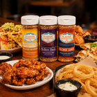 Three bottles of Flavor Expedition spices on a table with food in the background