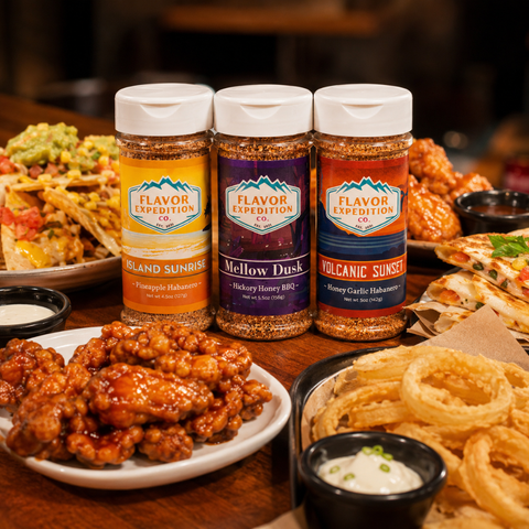 Three bottles of Flavor Expedition spices on a table with food in the background