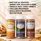 Three seasoning jars with labels 'Island Sunrise', 'Tuscan Evening', and 'Slow Noon' from Flavor Expedition Co. on a table with food.