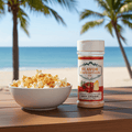 Bowl of popcorn and a bottle of Flavor Expedition Co. seasoning on a table with a beach background