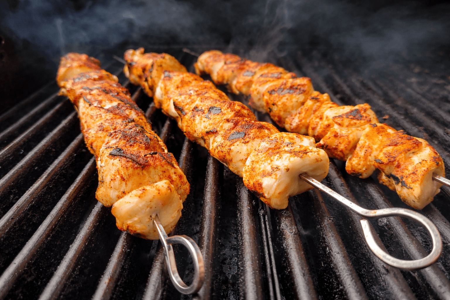 Skewers of marinated meat cooking on a grill with visible smoke.