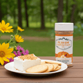 Bottle of Flavor Expedition Co. seasoning with a plate of cheese and crackers on a wooden table with flowers in the background.