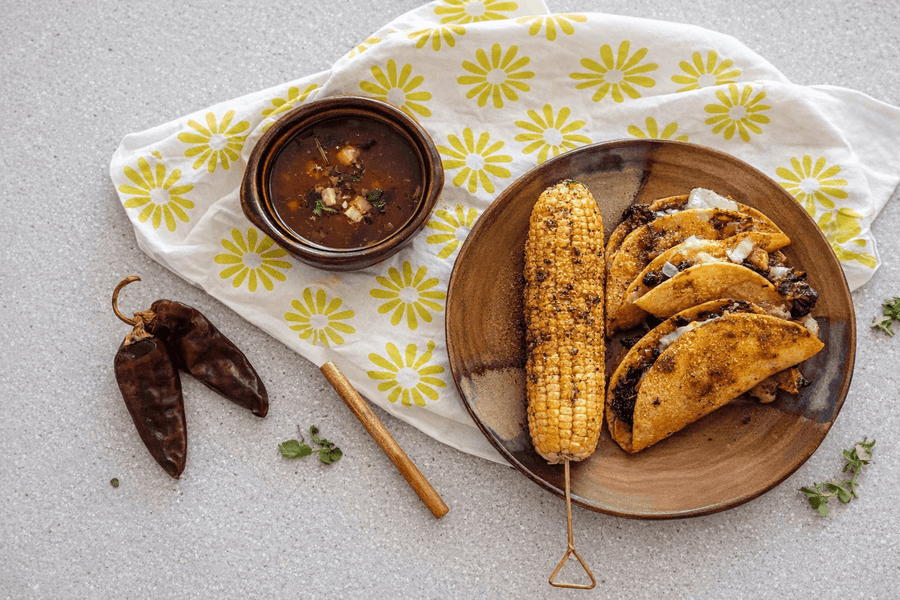 Plated meal with corn, tacos, and soup on a floral cloth