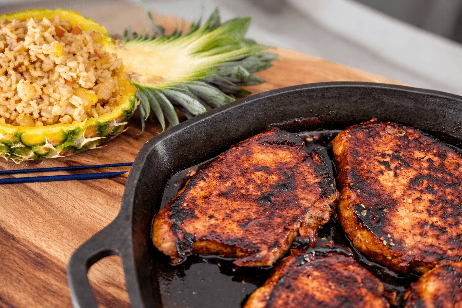 Grilled chicken in a cast iron skillet with a pineapple and rice on a wooden surface