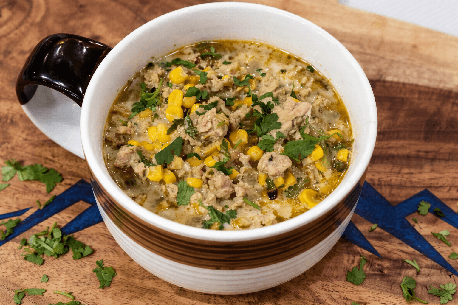  bowl of soup with ground meat, corn, and herbs on a wooden surface