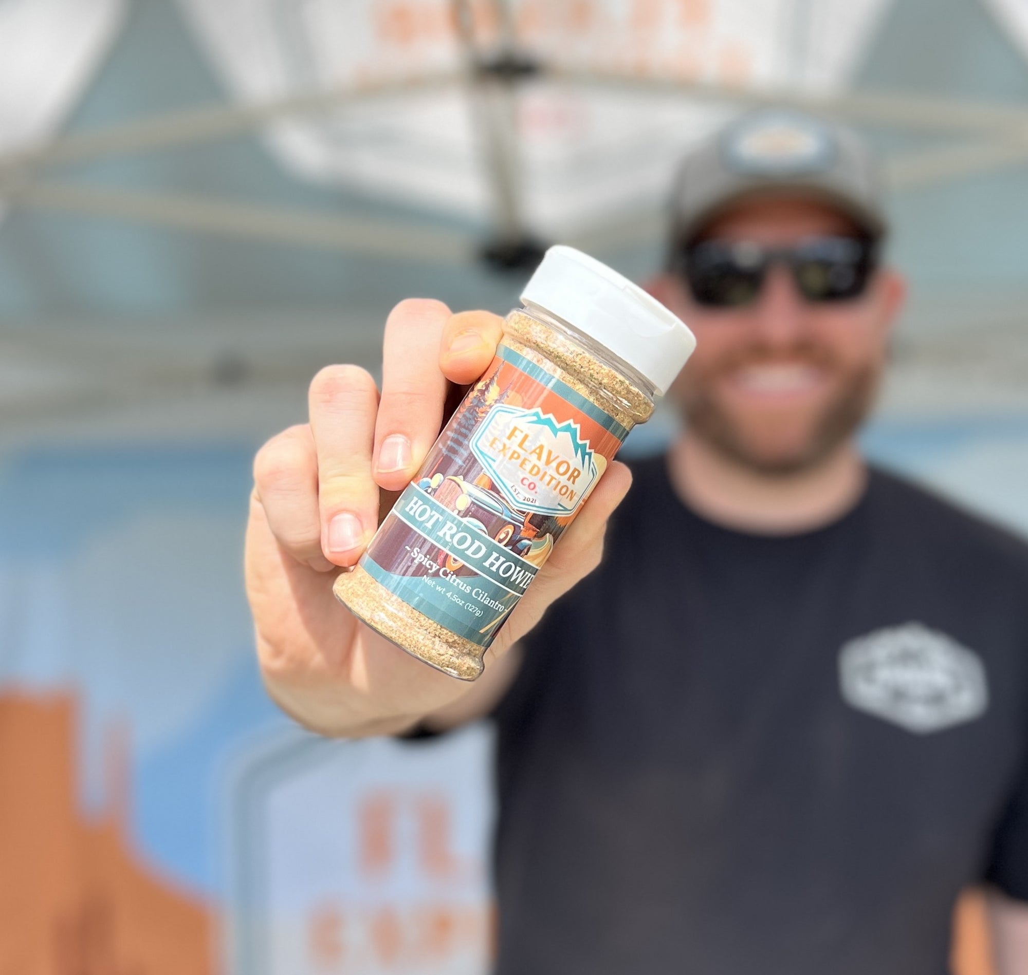 Person holding a jar of 'Lay On The Heat' hot pepper flakes with a blurred background