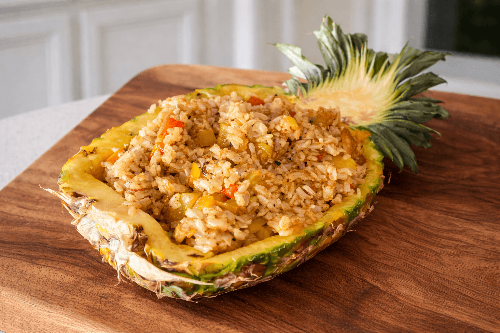 Pineapple filled with rice and vegetables on a wooden cutting board
