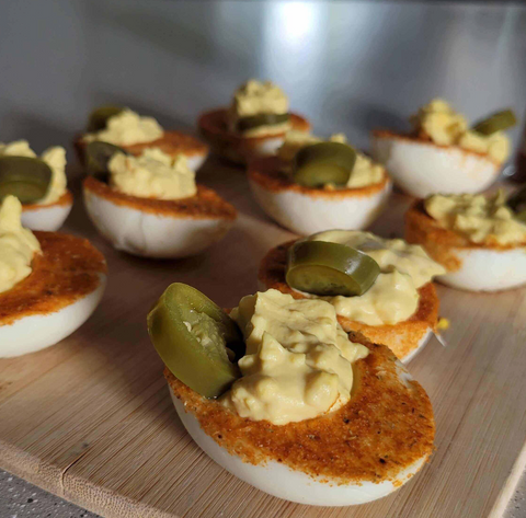 Delicious deviled eggs topped with pickled jalapeños on a wooden serving board.