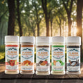 Five jars of Flavor Expedition Co. snack seasonings displayed in a sunlit forest setting.